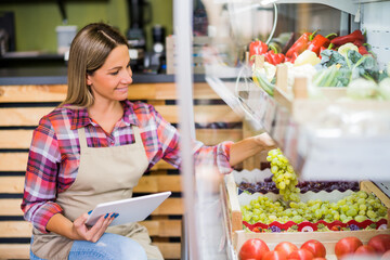 Woman works in fruits and vegetables shop. She is examining goods.