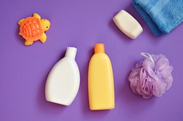 Baby cosmetics on a purple background. Natural shampoo, body lotion, sponge, soap bar, towel, rubber toy turtle. Bath products, toiletries set flat lay photography
