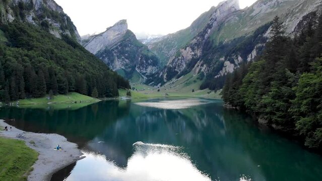 Aerial flyover low over the water of lake Seealpsee in Appenzell, Switzerland with a reflection of the Alpstein peaks on the lake's still surface