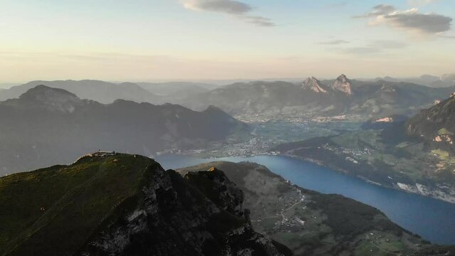 Aerial flight around the summit of Niederbauen Chulm on a golden summer evening in the Swiss Alps with a view of Mythen, Rigi, Burgenstock, Pilatus and glowing cliffs above Lake Lucerne