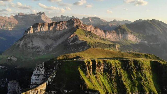 Aerial flight around the summit of Niederbauen Chulm on a golden summer evening in the Swiss Alps with a spinning view of the fjords of Lake Lucerne, Uri, Mythen, Rigi, Burgenstock and the setting sun