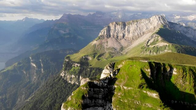 Aerial flyover over the summit of Niederbauen Chulm on a summer morning in the Swiss Alps with a view of the peak's cliffs rotating  towards Lake Lucerne's fjords