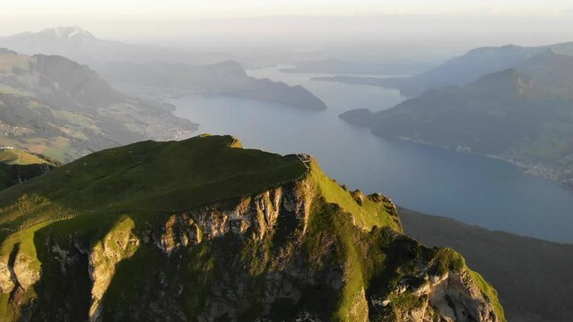 Aerial flyover over the summit of Niederbauen Chulm with a view of Lake Lucerne, Burgenstock and Pilatus in the background on a golden summer morning in the Swiss Alps