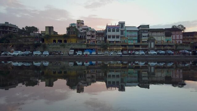 Parked Vehicles And Buildings On The Banks Of Godavari River At Dusk In Ramkund, Nashik, India. wide