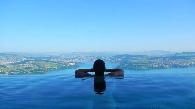 Woman Making a Heart Shape with Her Hands and Enjoy Infinity Swimming Pool with View over Mountain and Lake Lucerne in a Sunny Summer Day in Burgenstock, Nidwalden, Switzerland.