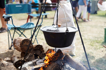 Outdoor cooking over a fire in a cauldron. We see an iron tripod with a cauldron and a hearth on it.