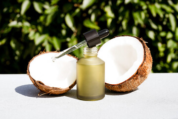 Mockup image of green glass dropper bottle with coconut cosmetic oil against natural green leaves background. Natural cosmetic treatment for skincare, coconut beauty products