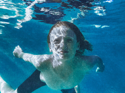 Young boy swimming underwater in blue ocean looking at camera