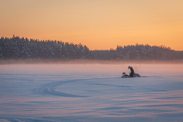 Amazing winter sunset in the forest with the orange sky, and snowmobile stuck in the snow