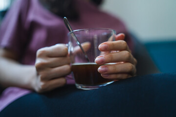 A close up of young woman hands holding cup of coffee while sitting in her chair relaxing during the day inside apartment 