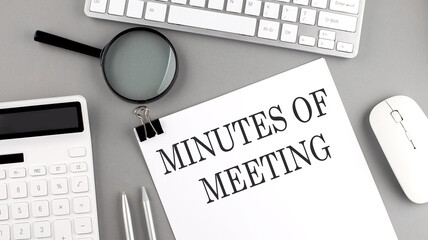 MINUTES OF MEETING written on paper with office tools and keyboard on the grey background