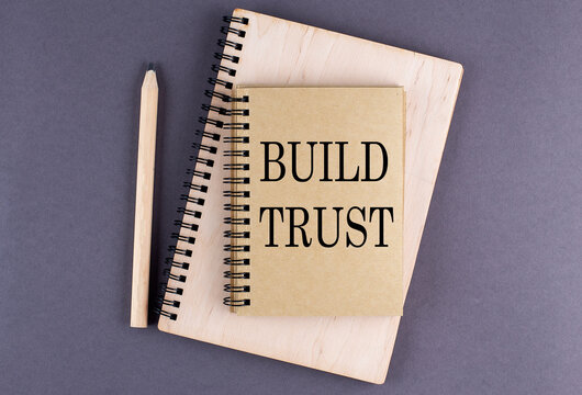 Word BUILD TRUST on notebook with pencil on the grey background