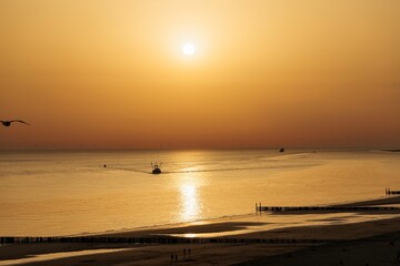 Beach scene with the sea waves reaching the sandy shore under the golden sunset sky