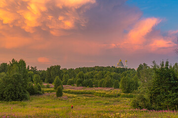 Summer sunset over the field with old monastery and stormy clouds