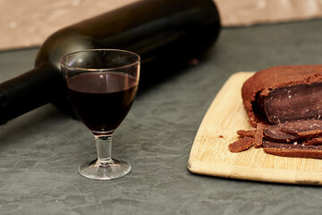 sliced basturma on a plate next to a bottle of wine and a glass