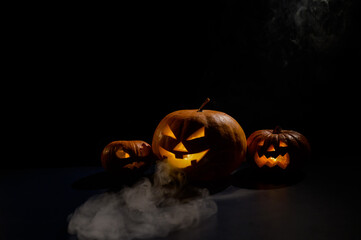 Pumpkins with carved grimaces and candles inside in the dark for halloween. Jack o latern in smoke.