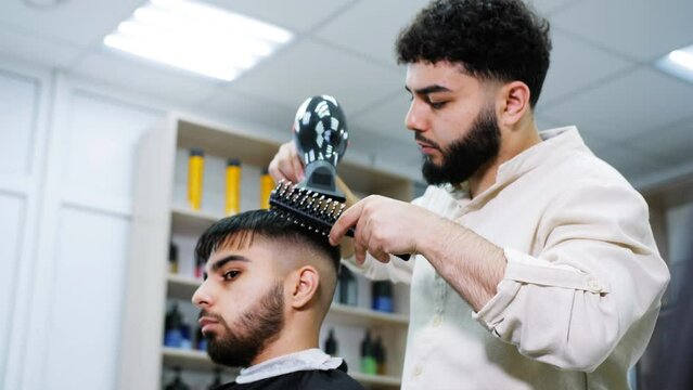 Barber blow-dries the hair of a client in a barbershop.
