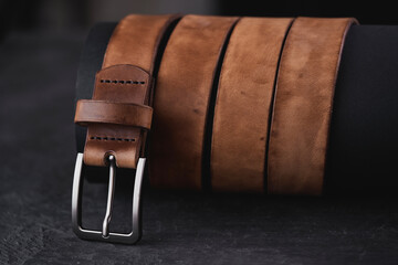 Fastened fashionable men's brown leather belt with a metal buckle on black background. 