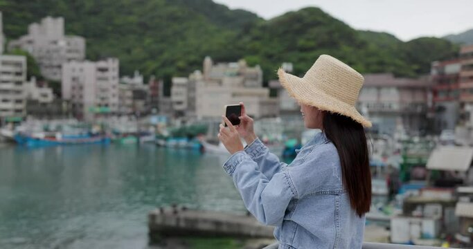 Travel woman use mobile phone to take photo at yehliu fishing harbor