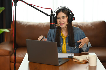 Beautiful woman wearing headphones using laptop and condenser microphone recording or streaming...