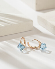 Golden earrings with square shaped light blue crystals and diamonds isolated on white background. Fashionable jewelry.