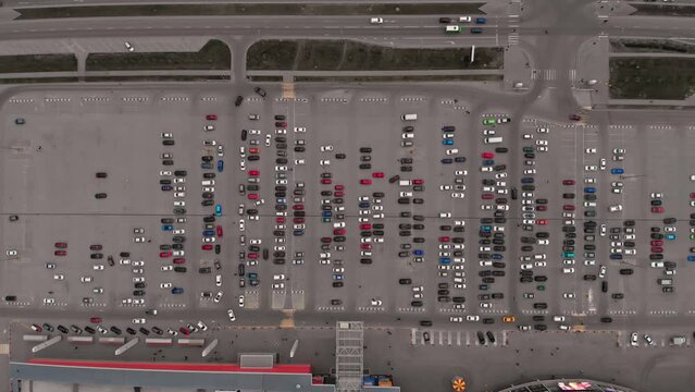 The drone flies over the parking lot with a lot of cars of different colors parked in the parking lot for the buyers of the mall Top view of cars that stand in the parking lot and move along the roads
