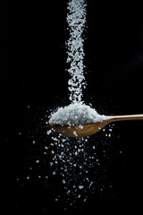 Obraz na płótnie Canvas Edible salt crystals falling down into the wooden spoon at black background.