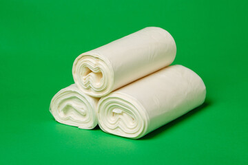 Close up of three rolls of white environmental garbage bags on green background.