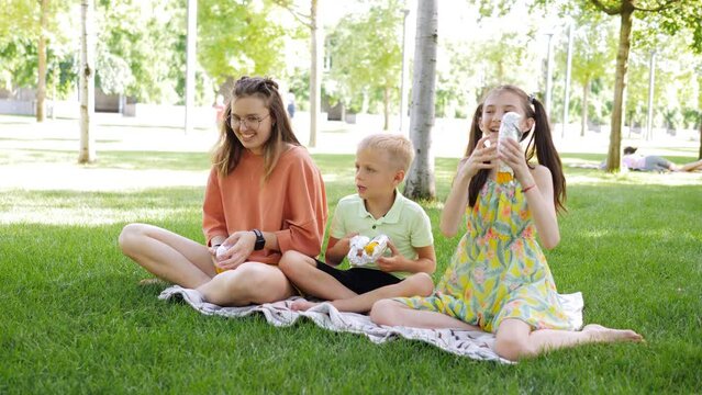 Happy children, a brother and two sisters, in the park on a picnic throw hot corn in foil playing.