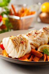 Fried pieces of cod loin, served with sweet potato fries. Light stone background.