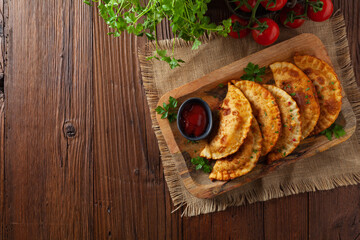 Traditional cheebureki, served on a wooden plate with sauce.