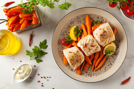 Fried pieces of cod loin, served with sweet potato fries. Light stone background.