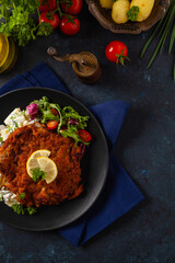 Classic, traditional Viennese sirloin schnitzel. Served on potato salad. Breaded. Dark background.