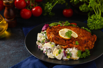 Classic, traditional Viennese sirloin schnitzel. Served on potato salad. Breaded. Dark background.
