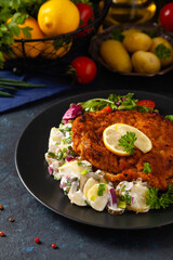 Classic, traditional Viennese sirloin schnitzel. Served on potato salad. Breaded. Dark background.