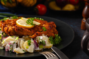 Classic, traditional Viennese sirloin schnitzel. Served on potato salad. Breaded. Dark background.