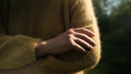 Female hand touching soft, yellow sweater from wool in sunlight
