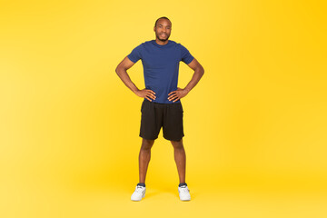 Fototapeta na wymiar Sporty Black Male Holding Hands On Hips Standing, Yellow Background