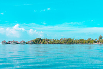 view from sea to island and water villas at day time with blue sky and beautiful clouds in the Maldives, the concept of luxury travel