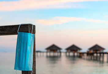 protective face mask against the water villas at sunset in the Maldives, the concept of luxury travel in new reality