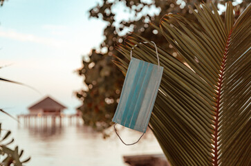 protective face mask against the water villas at sunset in the Maldives, the concept of luxury travel in new reality