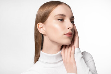 Fototapeta premium Beautiful girl touching her smooth soft facial skin. Model with natural makeup wearing white turtleneck. Skincare treatment cosmetics, beauty products.