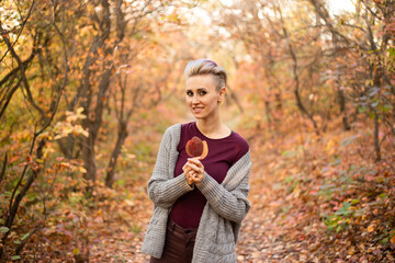 stylish woman with autumn leaf in autumn forest background with golden and red trees
