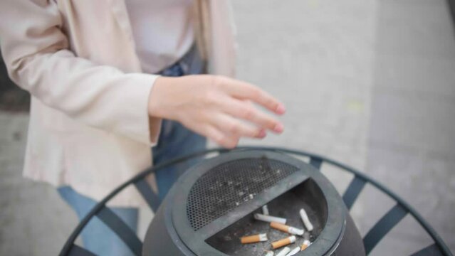 Woman throws cigarette into waste bin and quits smoking outdoors, closeup