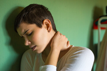 Young woman having neck pain leaning on the wall at home