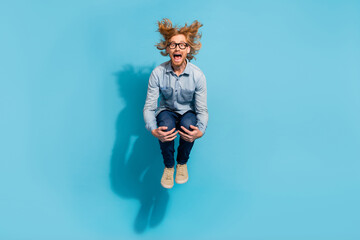 Full length photo of impressed funky man wear denim shirt spectacles jumping diving isolated blue...