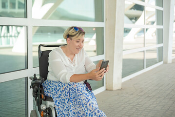 Fototapeta na wymiar horizontal portrait of a smiling Caucasian woman in a wheelchair looking at a cell phone
