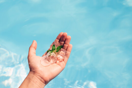 girl hand hold in hand palm some ice cubes and green mint leaves.mojito limonade cocktail concept.pool blue water background.sparkling surface summer sunny day.vacation family together.teenage girl