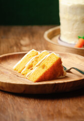 Slice of homemade carrot cake with cream cheese frosting on wooden plate on wooden background.