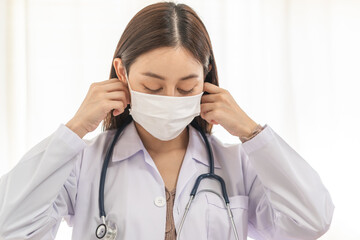 Doctor or physician asian young woman, wearing white coat, stethoscope and medical face mask to protect disease, prevention virus pandemic of covid-19, portrait isolated on background. healthcare.